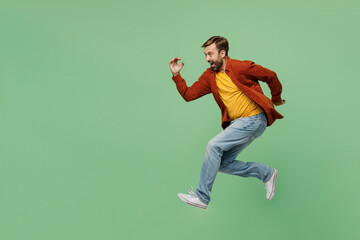 Full body side view happy fun cheerful elderly man 40s years old he in casual clothes red shirt t-shirt jump high run fast hurrying up isolated on plain pastel light green background studio portrait