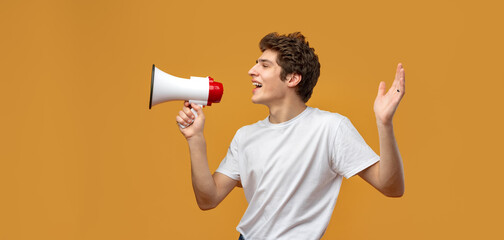 Young man shouting into megaphone making announcement against yellow background