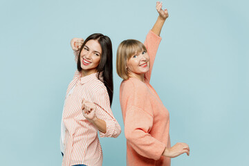 Side view smiling elder parent mom with young adult daughter two women together wearing casual clothes stand back to back dancing have fun isolated on plain blue cyan background. Family day concept.