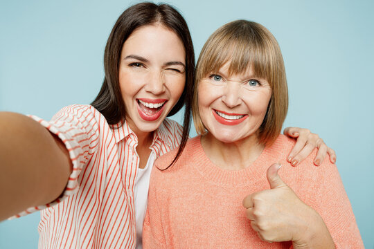 Close up elder parent mom with young adult daughter two women together in casual clothes doing selfie shot pov on mobile cell phone show thumb up isolated on plain blue background Family day concept