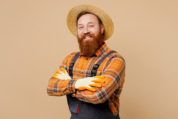 Confident fun young bearded man wear straw hat overalls work in garden hold hands crossed folded...