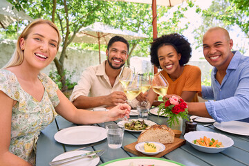 Portrait Of Group Of Friends Enjoying Outdoor Meal And Wine At Vineyard Restaurant With Cheers