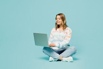 Full body smiling happy student young IT woman wear striped hoody sitting hold use work on laptop...