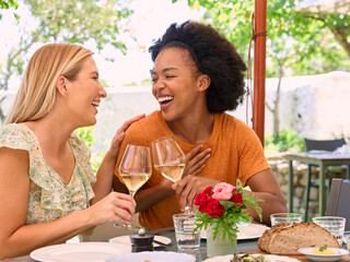 Two Female Friends Enjoying Outdoor Meal And Wine On Visit To Vineyard Restaurant With Cheers