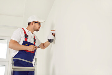 Video surveillance. Male worker installs surveillance cameras on wall for security in office or...