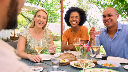 Group Of Friends Enjoying Outdoor Meal And Wine On Visit To Vineyard Restaurant