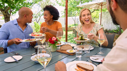 Group Of Friends Enjoying Outdoor Meal And Wine On Visit To Vineyard Restaurant