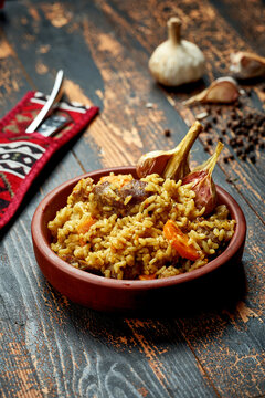 Classic pilaf with beef, garlic and carrots in a clay plate on a wooden background. Rustic