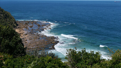 View from above of waves crashing onto rocky shore with trees in foreground