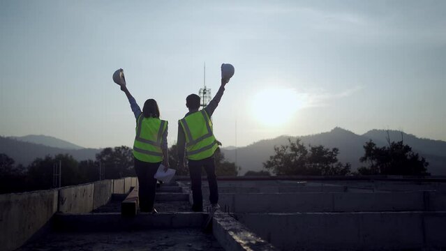 Silhouette of two engineers with helmets at construction site in background, sunset.