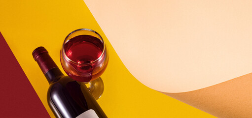 Bottle and glass of red wine on a yellow background. Sheet of paper for text. The image is grainy....