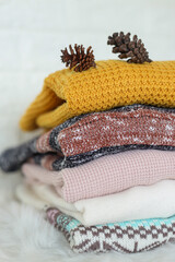 Stack of clean freshly laundered, neatly folded women's clothes on bedroom dresser's top. Pile of different sweaters of pastel colors in stack. Copy space, close up, background.