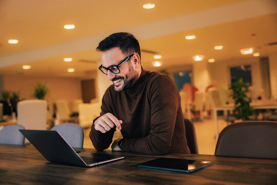 Smiling male boss having an online meeting over the laptop, sitting at the workplace.