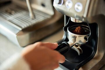 A woman is holding a coffee holder with ground coffee near a professional coffee machine.