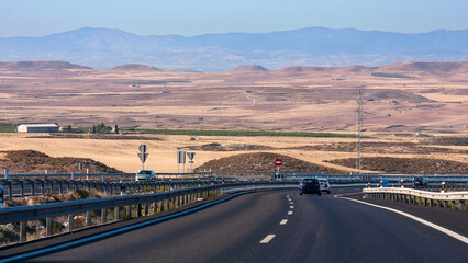 Highway in the middle of the dried fields with mountains in the background. Spain