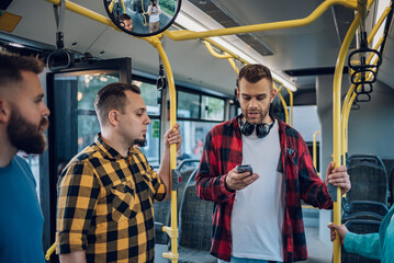 Couple of male friends talking and using a smartphone while riding a bus in the city