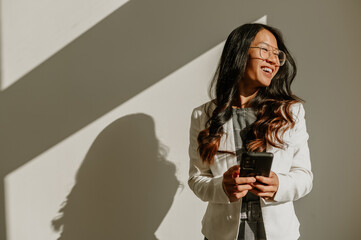 Asian businesswoman using smartphone while standing over a white wall in an office