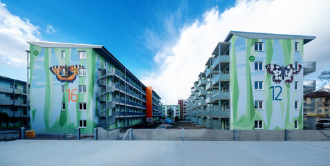 two modern apartment block buildings, artistic designed with a pattern of polygonal shapes, symbolizing floral elements and a painted Checkered butterfly and a large fox butterfly