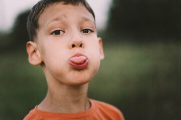 Portrait of a funny boy in a orange T-shirt and playing outdoors on the field at sunset. Happy child, lifestyle.