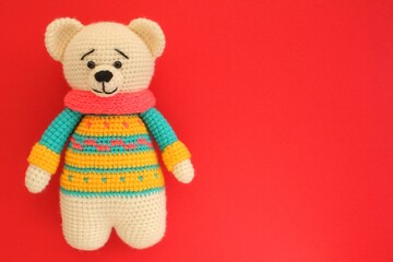 Crochet amigurumi handmade stuffed soft teddy bear toy in colored sweater on red background. Handwork, hobby. Craft diy newborn pregnancy concept. Knitted doll for little baby. Closeup flat lay out