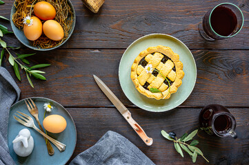 Easter food concept in farm rustic style. Egg, olive tree branch, crostata pie, red wine, decor on wood background. Top view