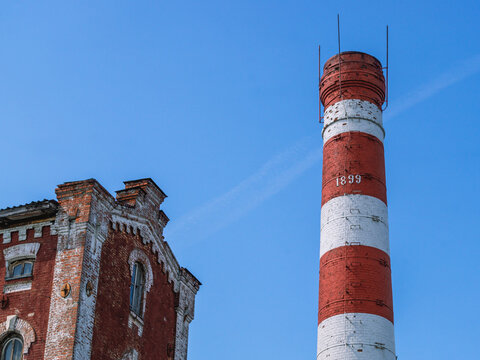 An old production pipe made of red brick, built in the 19th century. Industrial pipe with lightning rods. Brickwork of an old factory pipe.