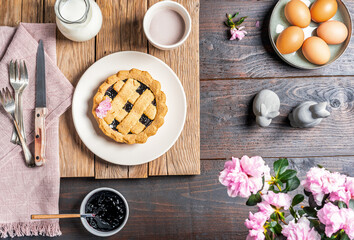 Easter food concept in farm rustic style. Eggs, crostata pie, cacao in mug, milk in jar, jam, rose napkin, easter decor over two wood backgrounds. Top view