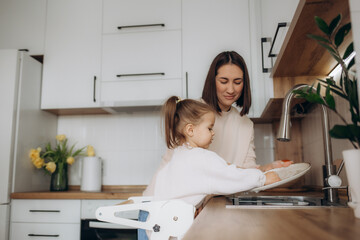 Mother and daughter washing dishes together in kitchen at home