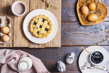 Fototapeta na wymiar Easter food concept in farm rustic style. Eggs, crostata pie, hot cacao in mug, milk in jar, jam, rose napkin, easter decor over two wood backgrounds. Top view