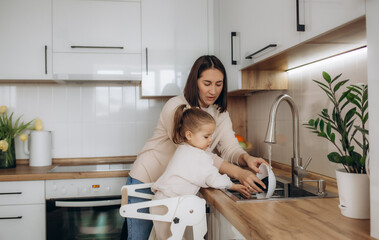 Mother and daughter washing dishes together in kitchen at home