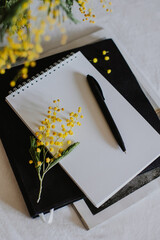Notebook with blank page, mimosa flowers and pen on a dark background.