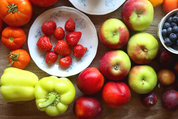Berries in vintage porcelain dishes, other healthy fruit and vegetable on wooden table. Top view.