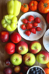 Berries in vintage porcelain dishes, other healthy fruit and vegetable on wooden table. Top view.