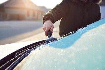 A man scratches the front window of his car on a cold winter morning