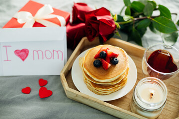Wooden tray with delicious breakfast - syack of pancakes, tea, present, roses and burning candle - 581747925