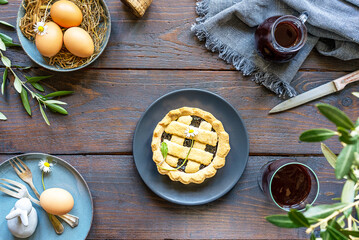 Easter food concept in farm rustic style. Egg, olive tree branch, crostata pie, red wine, decor on wood background. Top view