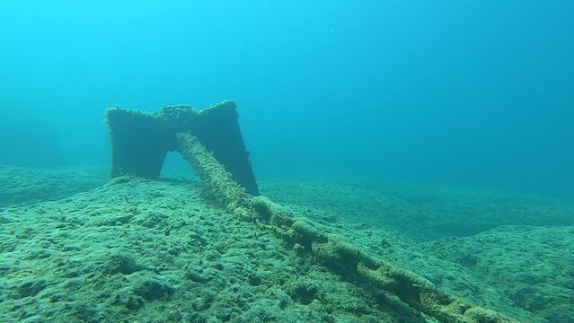 Anchor chain and anchor on the seabed. An anchor chain covered with algae stretches along the rock bottom.