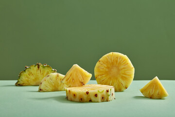 Pineapple slices and half slices decorated on minimalist green background. Blank space to display...