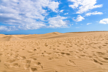 View of desert sand dunes against a moody cloudy blue sky. Maspalomas Dunes in Playa del Ingles, Maspalomas, Gran Canaria, Spain.