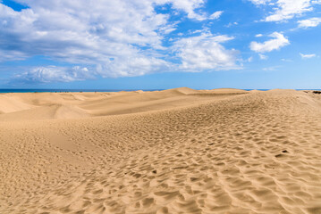 View of desert sand dunes against a moody cloudy blue sky. Maspalomas Dunes in Playa del Ingles, Maspalomas, Gran Canaria, Spain.
