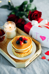 Mother's Day concept. Pancakes with berry, tea cup, burning candle, flowers and gift box.