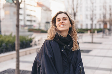 Happy blonde woman wear navy blue bomber jacket walking in the street and smiling to camera. Stylish girl in fashion outfit walking over the city. What a beautiful day out.