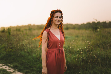 Portraits of a charming red-haired woman with a cute face. Girl posing for the camera in the field at sunset.