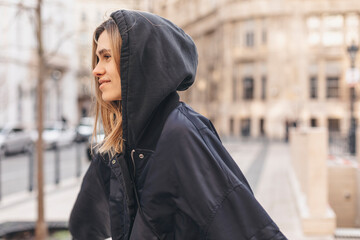 Attractive woman wear navy blue bomber jacket and hood walking on the street outdoor. Side view of...