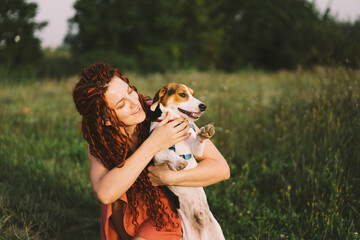 Beautiful woman plays with her Jack Russell dog in the park. The concept of animals, friendship, people and love. a woman lies on the grass and plays with a jack russell terrier