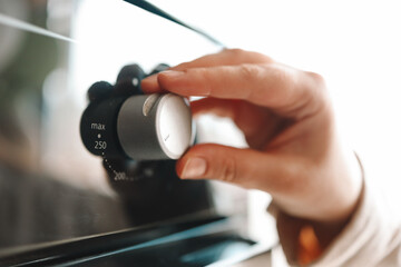 Women in modern kitchen turning on oven. Close up view of female hand and oven button