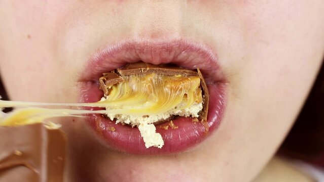 Hungry young woman biting and chewing a chocolate candy bar with nuts and nougat close up