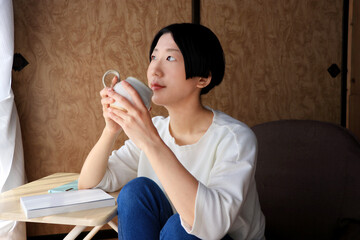 和室でのんびりコーヒーを飲む黒髪ショートヘアの若い女性