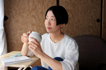 和室でのんびりコーヒーを飲む黒髪ショートヘアの若い女性