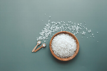 White sea salt in wooden plate on green background, home spa